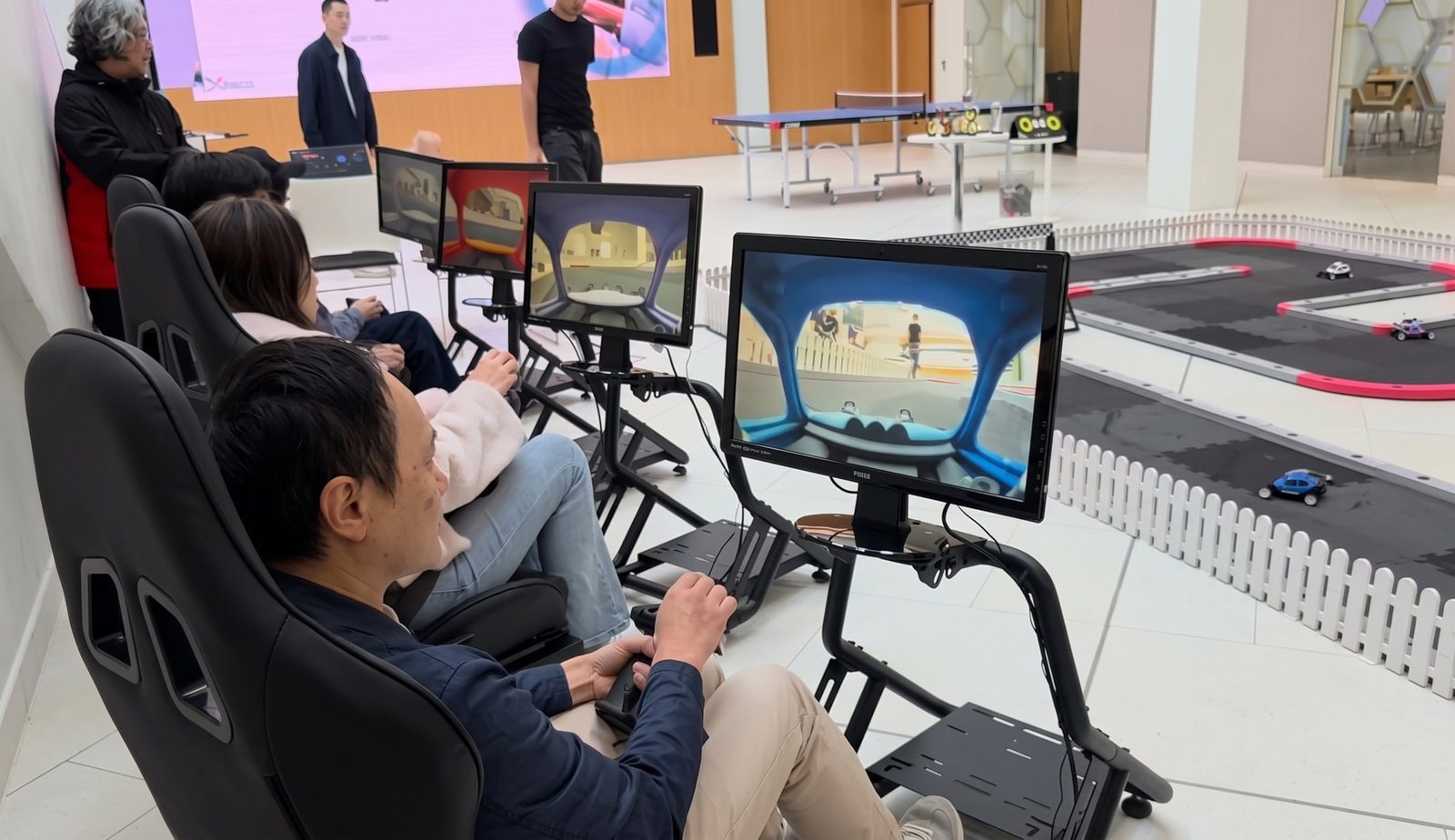 Drivers seated at screens showing each car's live onboard camera, holding RC controllers