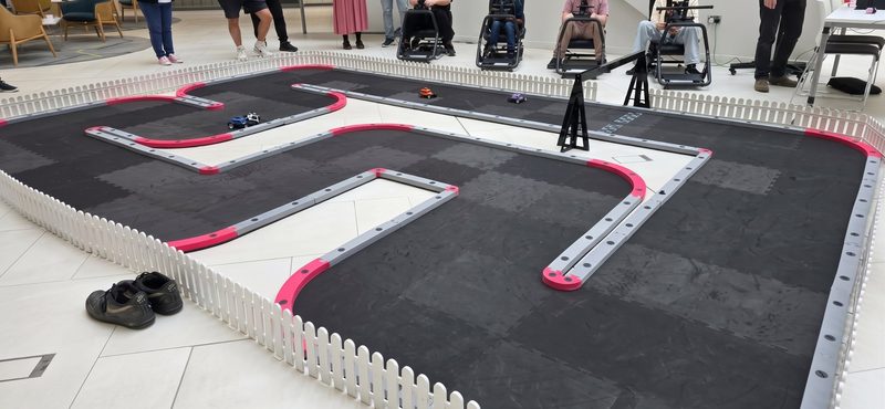 Wide view of the modular FPV RC track with pink and grey barriers and cars mid-race