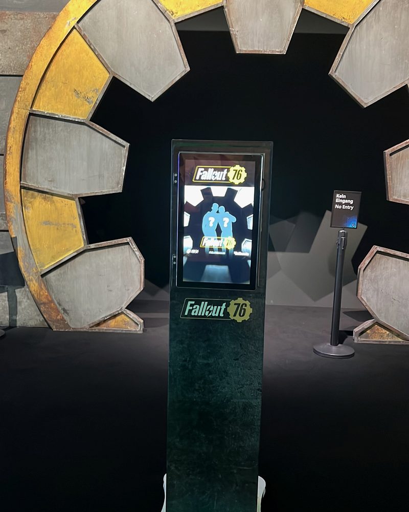 A themed, fully wrapped photobooth kiosk in front of a large set piece, its screen inviting guests to take their photo